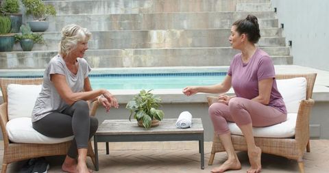Mature women chatting and relaxing by pool on rattan chairs in activewear
