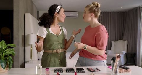 Friends sharing beauty tips with makeup kits in cozy bedroom