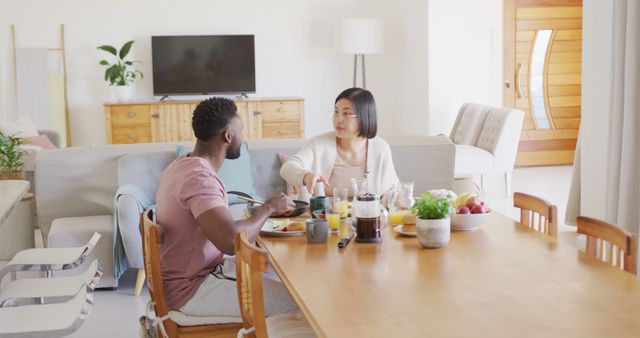 Happy diverse couple sitting at table and having breakfast. Spending quality time at home concept.