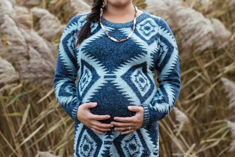 Pregnant woman embracing belly in knit sweater outdoors