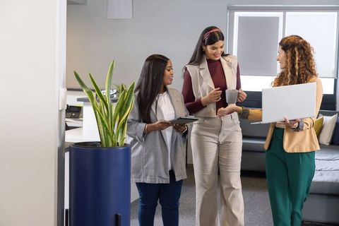 Female coworkers collaborating in modern office lounge holding laptop tablet and coffee