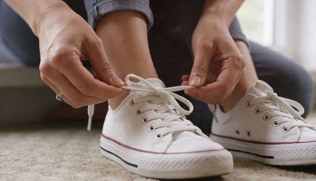 Tying white canvas sneakers on carpet wearing rolled jeans with ringed hand