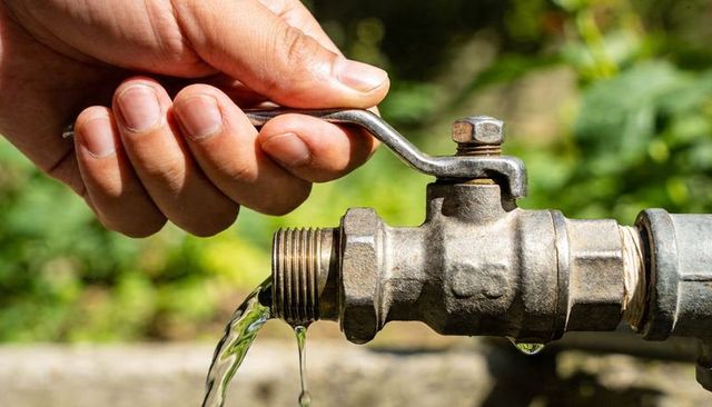 Hand turning outdoor garden faucet valve with flowing water droplets