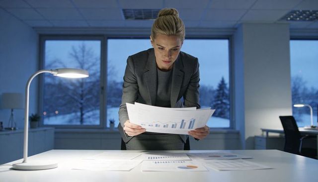 Executive reviewing financial charts during late-night work with snowy office view