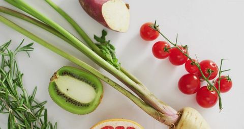 Fresh produce flat-lay featuring cherry tomato vine, halved kiwi, rosemary and citrus