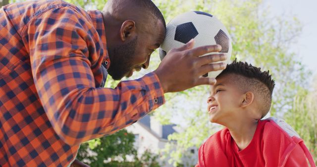 Father and son are enjoying their time together in a park by playing with a soccer ball. This image emphasizes family bonding, physical activity, and the joy of spending time outdoors. Ideal for advertising family-friendly products, parenting blogs, sports events, and recreational activities.