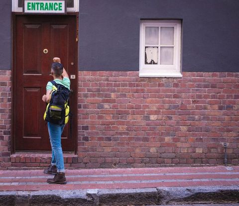 Backpacker knocking on wooden door of brick building