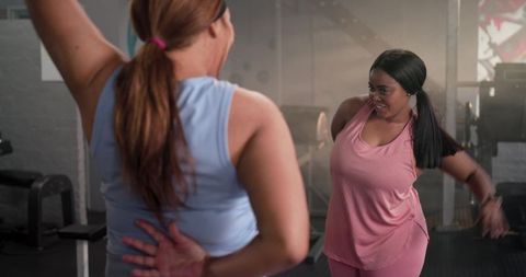 Women stretching in gym studio wearing pink and blue activewear, friends warming up together