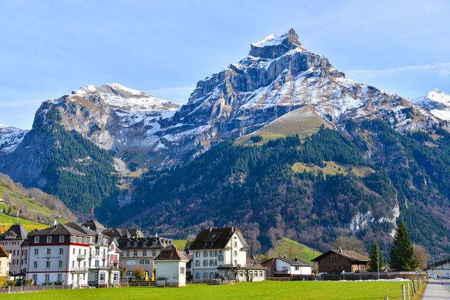 Captures serene winter landscape with snow-capped mountains towering over quaint alpine village with charming houses. Ideal for travel brochures, websites promoting mountain destinations, nature magazines, and calendars featuring picturesque landscapes.