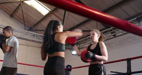 Female boxers training with focus mitts in boxing ring at urban gym, building fitness