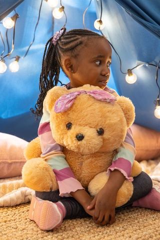 African american girl hugging giant teddy bear in cozy blanket fort with string lights
