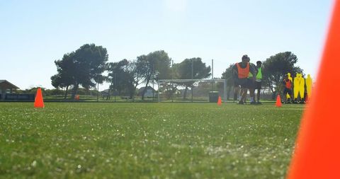 Grass-level soccer training session with players wearing bibs, cones and dummies