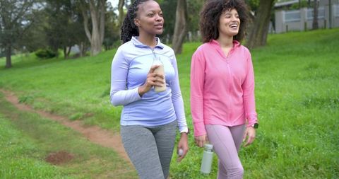 Diverse women walking in park carrying reusable bottles in activewear fitness stroll