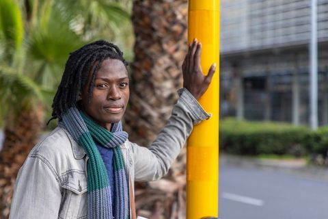 Mid adult african american man leaning on yellow pole on city sidewalk wearing denim jacket and scar