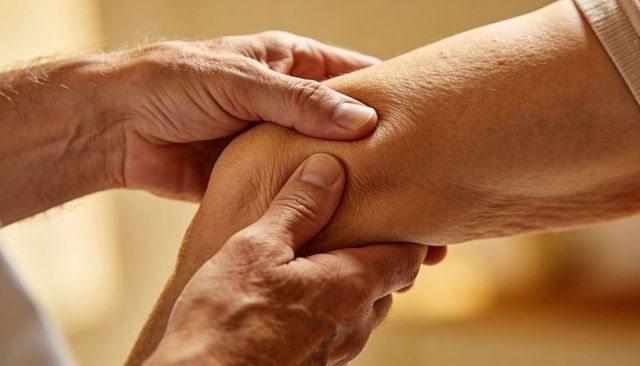 Caregiver hands providing gentle support to senior forearm closeup showing tenderness