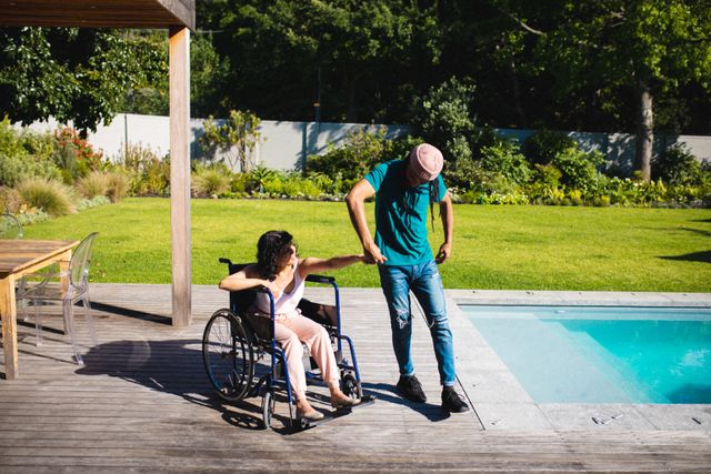 Full length of playful biracial man holding hand of disabled woman while dancing at poolside. love, disability and enjoyment, unaltered.