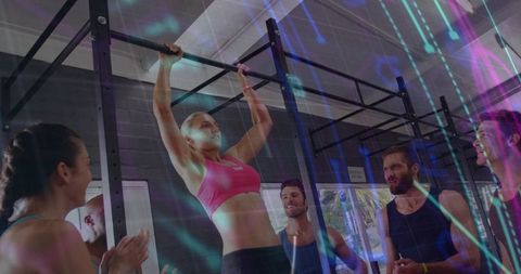Female athlete performing pull-up during group CrossFit class with coaches cheering