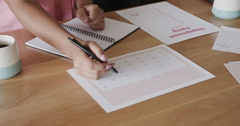Hands Scheduling Notes on a Calendar at Wooden Desk
