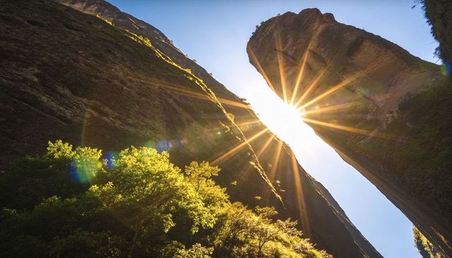 Sunburst streaming through vertical canyon gap with backlit trees and dramatic lens flare