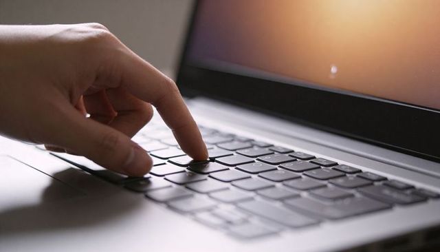 Fingertip Pressing Laptop Key on Chiclet Keyboard in Home Workspace with Warm Orange Glow