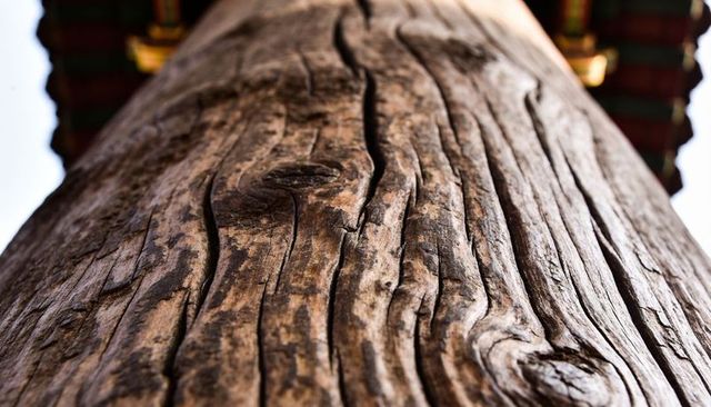 Weathered wooden column rising under painted eaves with deep grain, knots and cracks
