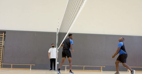Male teammates practicing volleyball on indoor court training wearing blue and black kits