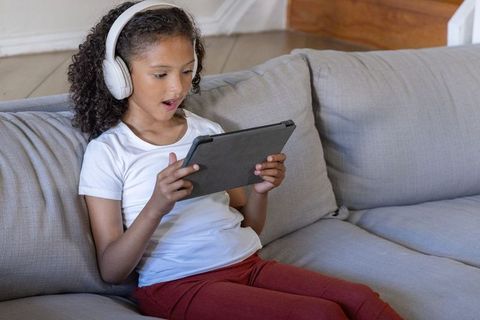 Girl wearing headphones on couch using tablet for online learning and play