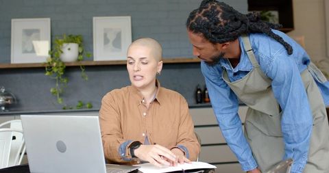 Diverse coworkers collaborating over laptop and paperwork in modern cafe workspace