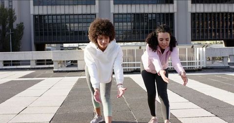 Diverse women stretching on rooftop terrace near office building for urban workout