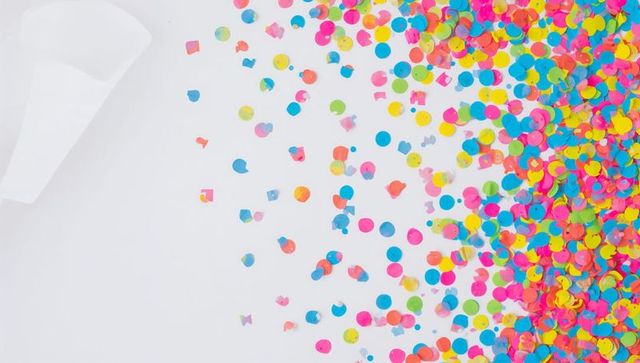 Vibrant neon confetti scatter on white background with curled paper cone flatlay party