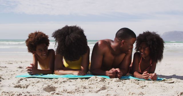 Portrait of african american parents and two children lying on a towel at the beach smiling. family outdoor leisure time by the sea.