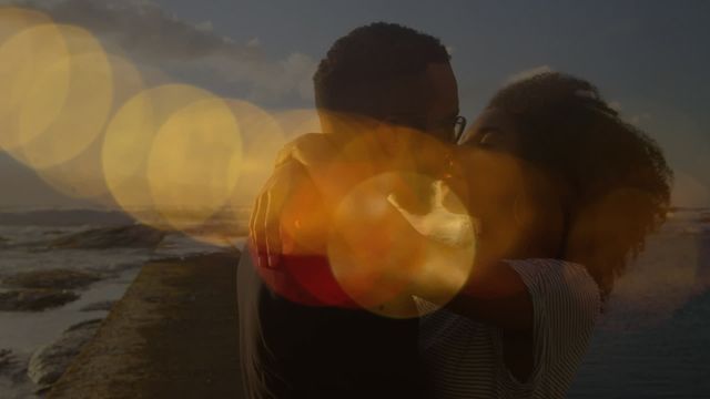 Diverse couple hugging and kissing on a beach during sunset, with warm lens flares adding a dreamy effect. Great for promoting love, romance, travel, vacations, advertisements for romantic getaways, and themes of warmth, togetherness, and happiness.