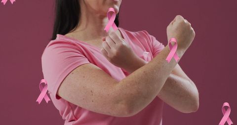 Woman in pink shirt standing against pink ribbon awareness