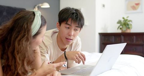 Young couple collaborating on laptop while lounging on bed in cozy bedroom