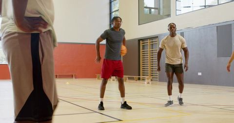 Black male teammates dribbling and passing during indoor basketball practice session