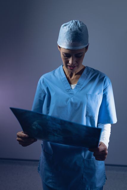 Female surgeon in blue scrubs examining an x-ray in an operating room at a hospital. Ideal for use in medical, healthcare, and hospital-related content, including articles, websites, and educational materials.