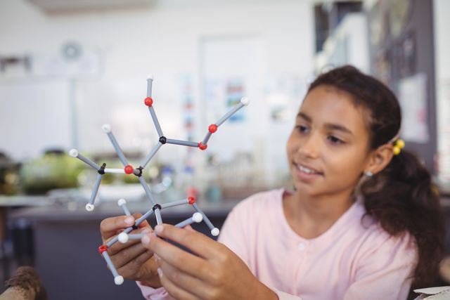 Young girl engaging in hands-on learning with a molecule model in a science laboratory. Ideal for educational materials, STEM program promotions, school brochures, and science-related articles.