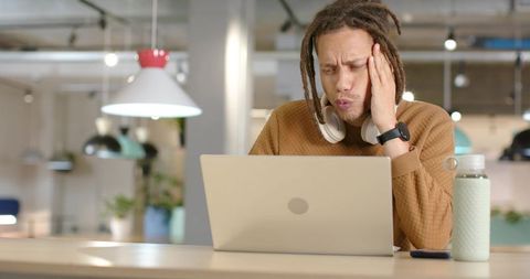 African American man holding head while concentrating on laptop in modern coworking space