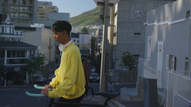 Depicts a fashionable biracial transgender adult wheeling a bicycle through a city on a sunny summer day. Useful for urban lifestyle, fashion trends, inclusive communities, and city living concepts.