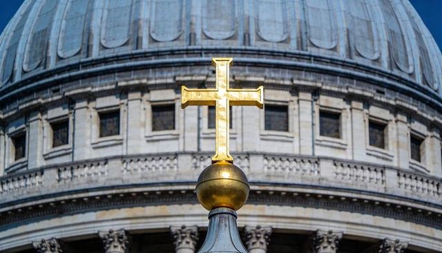 Glinting gilded cross and orb atop cathedral dome reflecting sunlight on neoclassical architecture