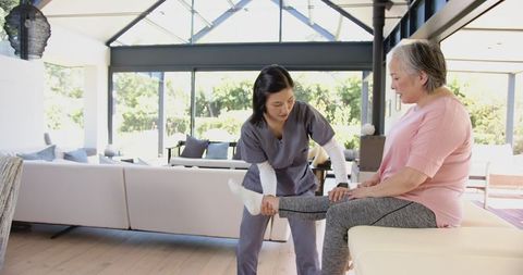 Physiotherapist Assisting Senior Woman with Leg Exercises at Home