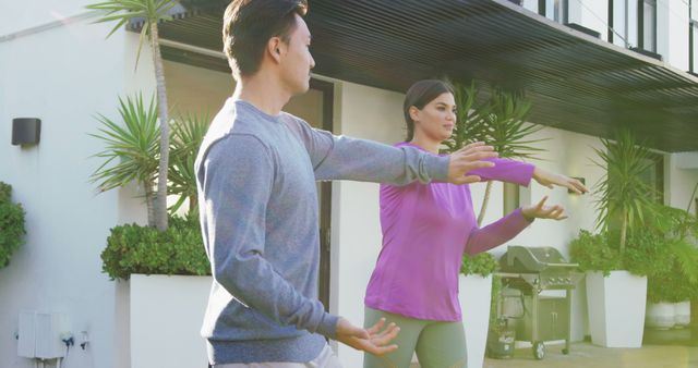 Image of relaxed diverse couple exercising tai chi in garden. leisure, relax, active lifestyle and spending free time at home and garden concept.
