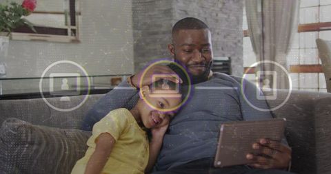Father and daughter bonding while watching tablet on couch during cozy family time