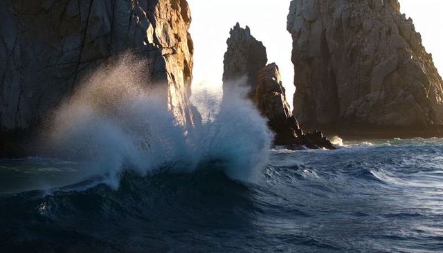 Sunlit waves crashing against rocky headland with dramatic sea spray