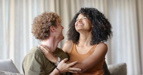 Young couple laughing and embracing on sofa, cozy intimate home moment of joy, connection
