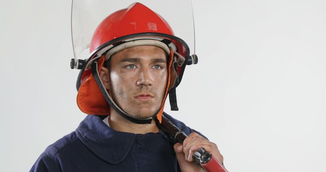 Focused biracial male firefighter wearing hardhat, protecting suit and holding tool, copy space. Fire prevention, professionals, tool, safety and expression concept, unaltered.