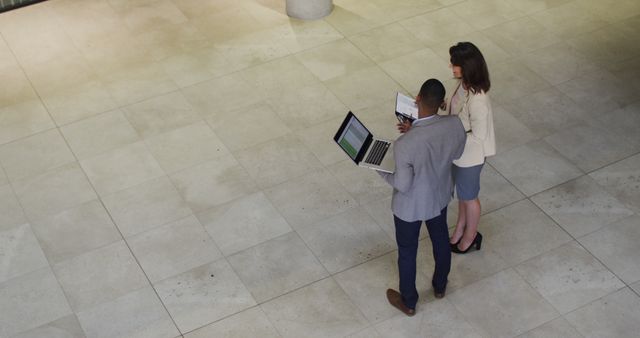 Diverse businessman and businesswoman talking and using laptop in lobby of modern office. business and business people in office concept.