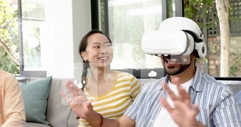 Man Wearing VR Headset Reaching Out While Woman Watching and Smiling in Modern Living Room