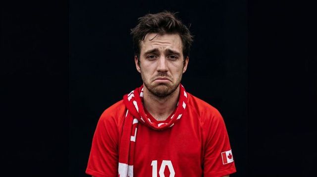 Solemn canadian soccer fan frowning in red jersey number 10 wearing scarf