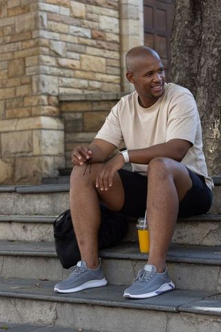 African american man relaxing on steps with sunglasses and orange juice near masonry entrance